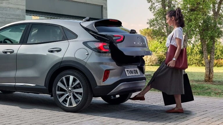 Main tenant des clés de voiture devant véhicule garé en extérieur, geste de remise ou récupération de clés automobiles