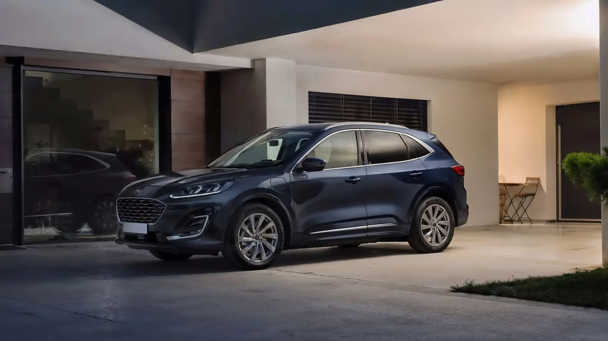 Véhicule SUV bleu métallisé stationné sur une plage au coucher de soleil, avec un ciel aux teintes roses et orangées se reflétant sur l'océan calme à l'horizon