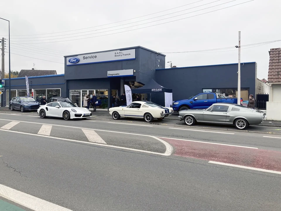 M&eacute;canicien automobile en combinaison bleue et casquette inspectant un moteur de voiture, capot ouvert dans un garage
