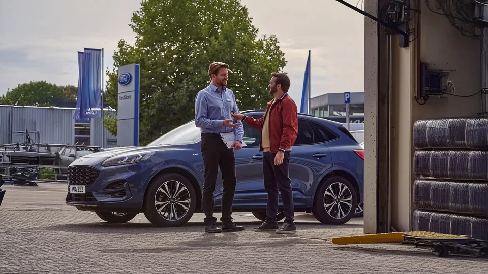 Atelier de carrosserie automobile intérieur avec technicien en combinaison de protection blanche et masque respiratoire appliquant peinture rouge sur véhicule